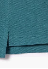 Teal-punainen puuvillakangas, jossa on teksturoitu pinta, hemmin reuna ja sivuaitauksen yksityiskohta joustavuutta ja tyyliä varten.