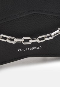 Czarna torebka z teksturowanej skóry z srebrnym łańcuszkiem oraz wyciskiem logo „KARL LAGERFELD”. Geometryczny design z przeszytymi krawędziami.