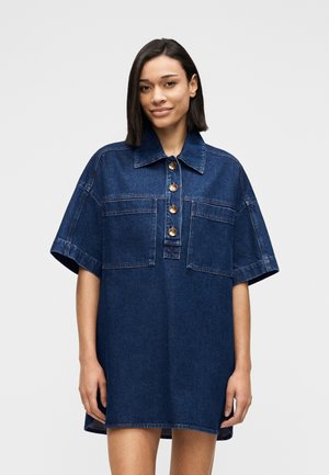 Robe-chemise en denim avec un col à revers, des manches courtes, une patte de boutonnage à l'avant avec des boutons dorés, et deux poches sur la poitrine.