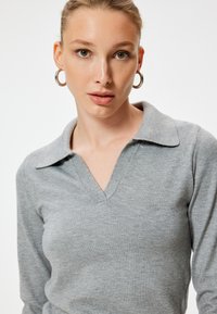 Grijze pullover met een V-hals, lange mouwen en een zachte, gladde textuur. Voorzien van ribgebreide accenten op de hals en manchetten.