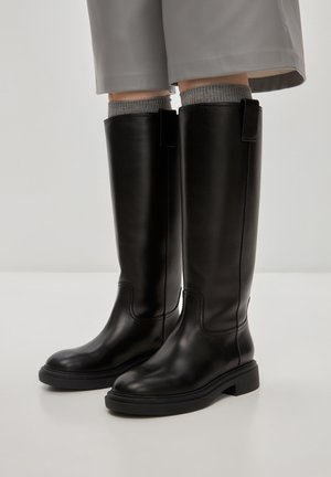 Bottes noires en cuir, montantes jusqu'au genou, avec une finition lisse, un bout rond, une semelle en caoutchouc contrastée et des détails de couture minimaux.