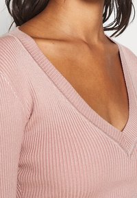 Roze geribbelde gebreide top met een V-halsontwerp. Heeft een getailleerde pasvorm en een soepele structuur, met stikdetails langs de halslijn.