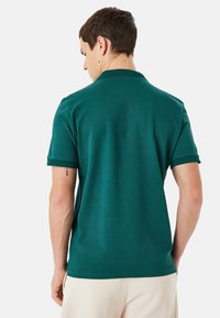 Grön kortärmad polo med en texturerad krage och ärmslut. Materialet verkar slätt med en subtil lyster och skräddarsydd passform.