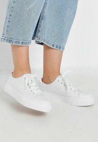Vita canvas sneakers med rund tå, platt sula och snörningsdesign. Har en texturerad tyg och en subtil logotyp nära snörhålen.