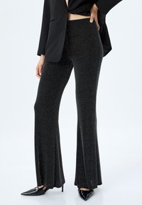 Uitgebreide zwarte broek van glinsterende stof, met een gladde textuur en een aansluitende taille, gecombineerd met spitse zwarte hakken.