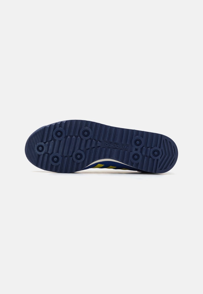 Blauer Gummi-Sneaker-Boden mit strukturiertem Oberflächen, kreisförmigen Grip-Mustern und einer weißen Zwischensohle mit gelben Akzenten an der Seite.