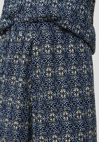 Robe en coton ornée d'un motif floral géométrique bleu, blanc et jaune, avec une texture douce et une taille froncée pour une silhouette fluide.