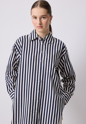 Button-up shirt with long sleeves, made of lightweight fabric, featuring vertical navy and cream stripes, a curved hem, and a chest pocket.