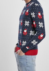 Pull de Noël bleu marine avec des flocons de neige blancs et des Pères Noël rouges, fabriqué en tricot, avec un bas et des poignets côtelés rouges.