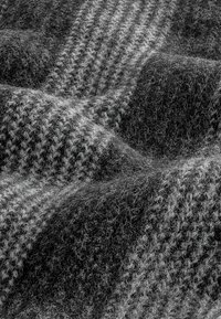 Vlněná deka s černobílým houndstooth vzorem, s měkkým, texturovaným povrchem a viditelnými vlákny, která vytvářejí útulný vzhled.
