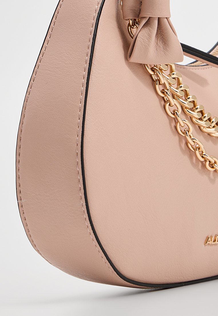 Sac à main en cuir rose blush avec une forme arrondie, des détails noirs, des accents en chaîne dorée et un petit nœud sur la poignée.