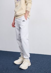 Lys grå joggebukser laget av bomull, med sidelommer, elastisk liv, og en liten svart logo. Kombinert med beige sportsko.