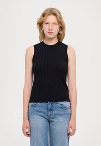 Top nero senza maniche in maglia con motivo testurizzato e scollatura rotonda, abbinato a jeans azzurri a vita alta.