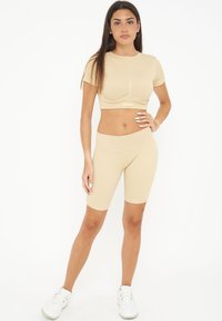 Beige ribbet cropped top med korte ærmer, parret med matchende high-waisted cykelshorts. Modellen har hvide sneakers på. Glat tekstur.