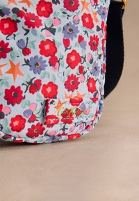 Blommönstrat tyg med röda, lila och orange blommor på ljusblå bakgrund, med en sydd Cath Kidston-etikett.