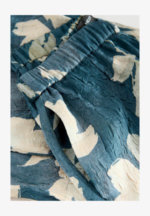 Ryppyiset, petroolinvihreät housut, joissa on valkoiset abstraktit kuviot, kuminauhavyötärö ja sileä pinta.