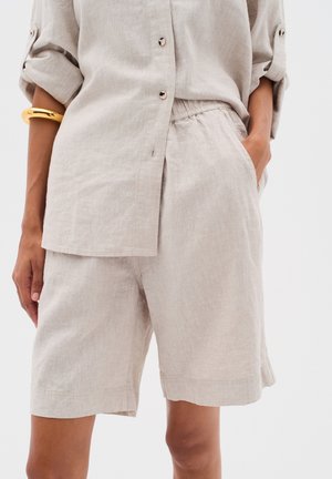 Chemise en lin avec une coupe décontractée, de couleur beige clair, à boutons sur le devant et manches retroussées ; assortie à un short beige avec une taille élastique.