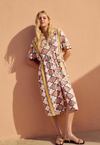 Abito a maniche corte e lunghezza ginocchio di colore rosa chiaro con motivi geometrici in marrone, blu e giallo. Dotato di una cintura in vita per una vestibilità perfetta.