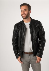 Giacca bomber in pelle nera con una trama liscia, chiusura con zip e colletto a coste. Indossata sopra una t-shirt grigia e jeans grigio chiaro.