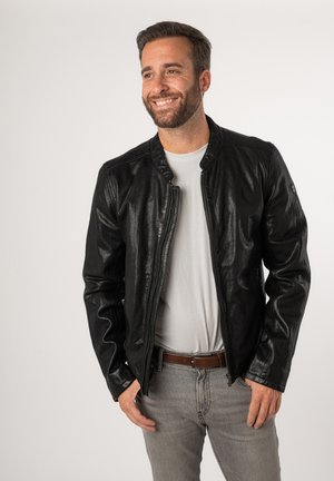 Schwarze Lederbomberjacke mit glatter Textur, Reißverschluss und geripptem Kragen. Getragen über einem grauen T-Shirt und hellgrauen Jeans.