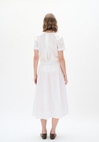 White cotton dress with short sleeves, elastic waist, and flowing skirt. Features a back closure detail and lightweight texture.