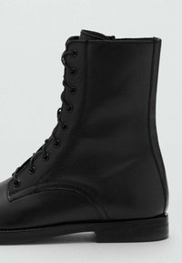 Botín de cuero negro hasta el tobillo con punta redonda, suela plana y cordones con ojales. Textura suave con un detalle de costura mínimo.