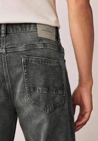 Gray denim jeans with a straight cut, featuring a back pocket with stitching detail and a branded leather patch at the waist.