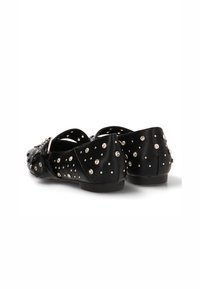 Zapatos planos negros de cuero suave, con tachuelas plateadas en la parte superior y un tacón bajo. Diseño clásico con un ajuste cómodo.