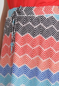 Falda de colores con un diseño geométrico que presenta flechas rojas, negras, azules y azul claro. Se ajusta con un cordón azul en la cintura.