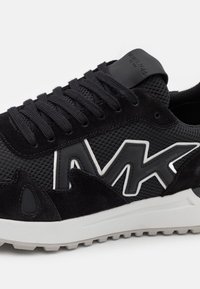 Černá teniska s materiály z síťoviny a semiše, gumovými detaily, výrazným logem a texturovanou podrážkou pro lepší trakci.