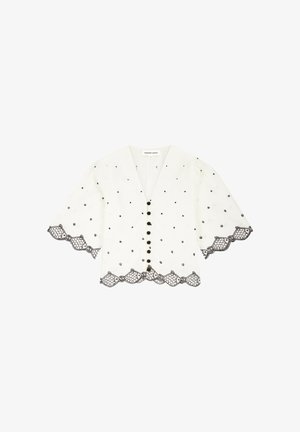 Witte blouse met zwarte polkadots, geschulpte kanten rand aan mouwen en zoom, knopen aan de voorkant en een V-halskraag.