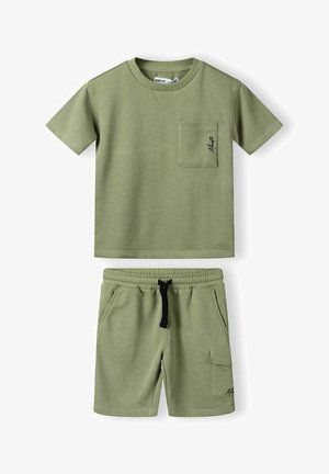 Lys grøn bomulds skjorte med korte ærmer og lomme samt matchende shorts. Shortsene har en elastisk talje og en sidelomme. Sorte detaljer.