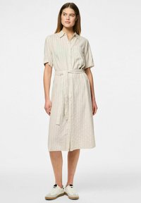Abito camicia beige chiaro con maniche corte, righe verticali, bottoni frontali e una cintura abbinata; abbinato a sneakers bianche.
