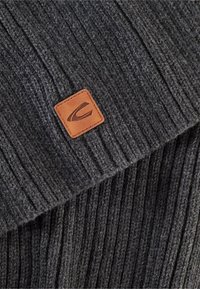 Dark gray knitted beanie with a ribbed texture and a rectangular leather patch featuring a logo. Smooth fabric with a cozy appearance.