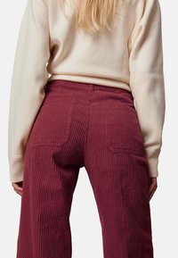 Bordeaux corduroy broek met verticale ribbels, met twee achterzakken. Gepaard met een lichtbeige trui, die een textuurstof toont.