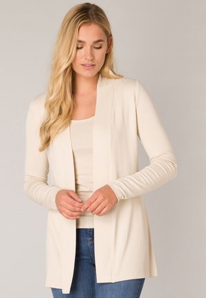 Beige cardigan, open front, lange mouwen, zachte stof, lichtgewicht. Draag het over een bijpassende top, gecombineerd met blauwe jeans.