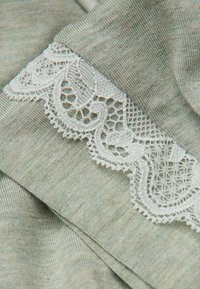 Tejido de color verde claro con un punto texturizado, acentuado con un borde de encaje blanco a lo largo del borde, que muestra patrones y detalles intrincados.