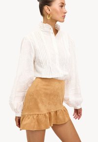 Witte reliëf blouse met rimpel-kraag, knopenlijst en pofmouwen, gecombineerd met een tan suede mini-jurk met een gerimpelde zoom.