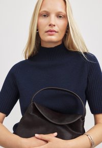 Tumes ribikoot lühikeste varrukatega; hoiab tumeda pruuni pehme nahkrahakotiga, millel on kaarjad klapid ja silmus käepide.