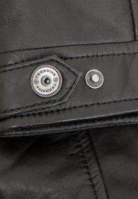 Schwarzes Ledergewebe, das eine detaillierte Nahaufnahme eines Druckknopfverschlusses und eines Etiketts mit "redpoint" zeigt. Es hat eine glatte Textur und Nähte.