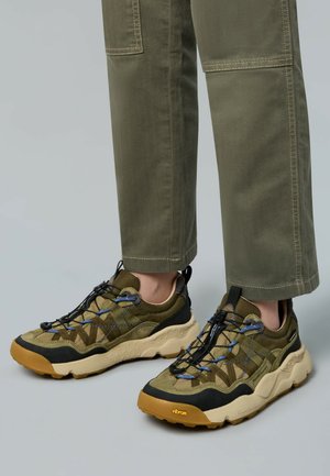 Olivgrüne Sneaker mit schwarzen Akzenten, einer strukturierten Oberseite und einer klobigen Sohle. Verfügt über ein Schnürsystem und Vibram-Branding auf der Sohle.
