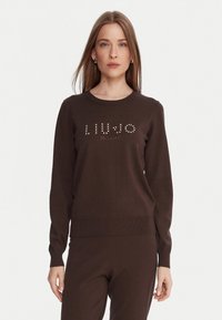 Maglione marrone a maglia con maniche lunghe, caratterizzato dal testo "LIU∙JO MILANO" adornato con strass sul petto. Orlo e polsini a coste.