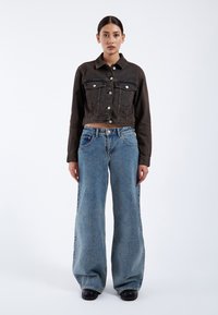 Dark cropped denim jacket with button closure, front pockets; paired with loose-fitting light blue jeans, black platform shoes.