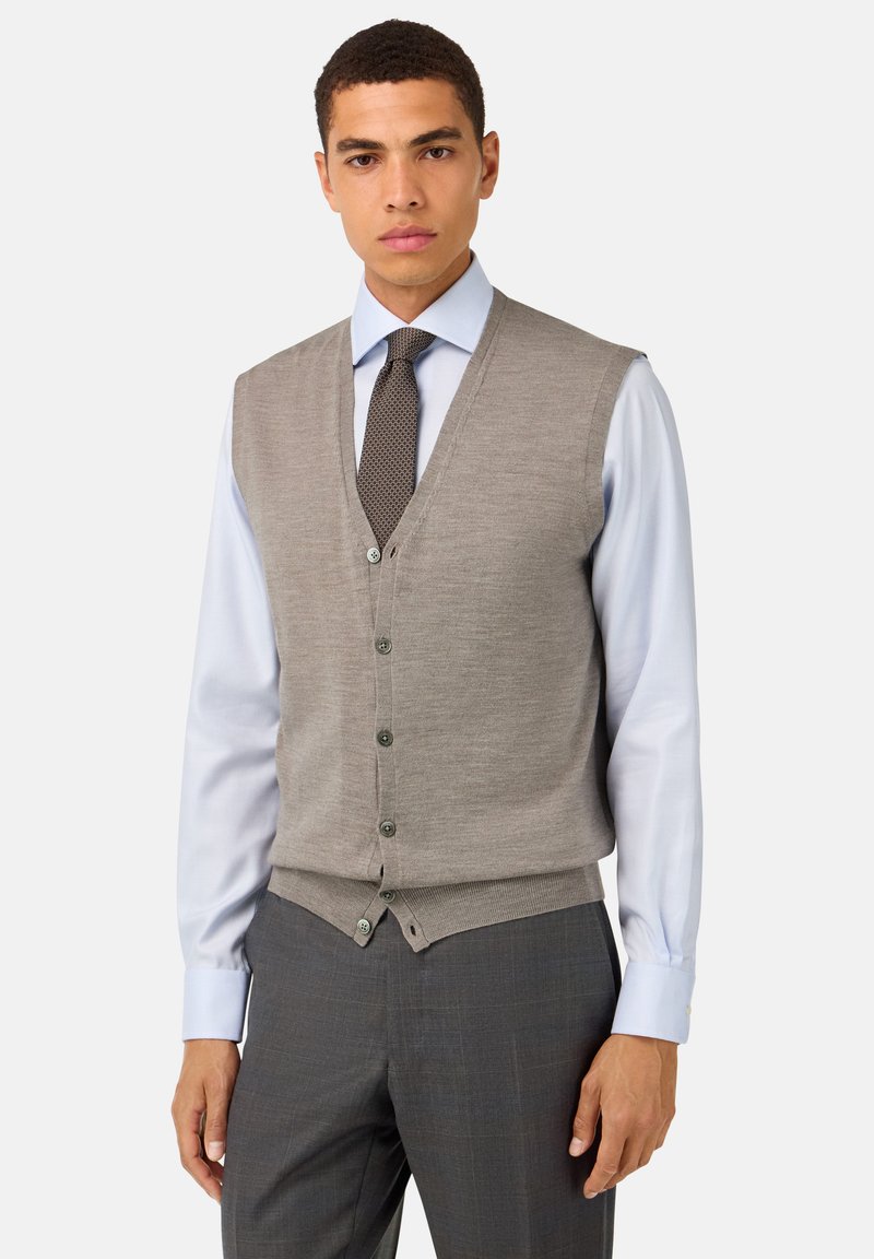 Svetlošedý vest, vyrobený z vlny, s výstrihom do V, päťgombíkovým zapínaním a kontrastnými gombíkmi. Nosený cez svetlomodrú košeľu.