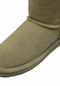 Karamelli suede'ist pahklai, ümarate varvastega, minimaalse õmbluse detailiga ja lame kummitald, millel on sile ja pehme tekstuur.
