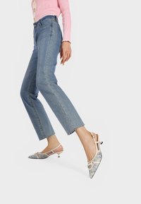 Décolleté beige con tacco a pantofola e punta affilata, caratterizzati da un motivo decorativo e un tacco piccolo. Indossati con jeans cropped azzurri chiari.