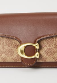 Portefeuille en cuir marron avec un devant en toile texturée beige, doté d'un fermoir doré et d'accents de couture, de forme rectangulaire.
