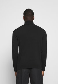 Jersey negro de cuello alto con mangas largas, con un cuello y puños acanalados, hecho de una tela suave, que presenta una textura lisa y un diseño ajustado.