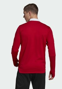 Rotes langärmeliges Sporthemd mit weißem Kragen, das eine glatte Textur und eine figurbetonte Form aufweist. Beinhaltet Daumenlöcher an den Bündchen.