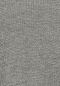 Svetlo sivi pleteni pulover s teksturiranim vzorcem, ki vsebuje prepletene niti in ohlapno, sproščeno šivano zasnovo.